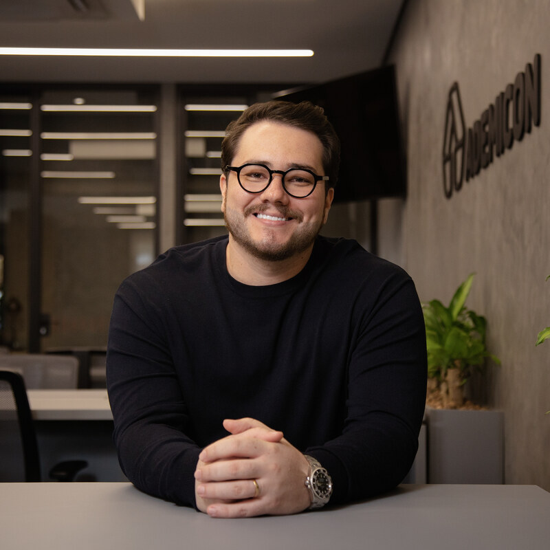 Andrews Lacar, Diretor Licenciado da Ademicon Alto da Boa Vista, em frente ao logo Ademicon iluminado.